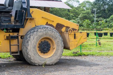 Sarı bir yol silindirinin yan görüntüsü. Gün ortasında parktaki rulo olmadan tribünde duruyor.