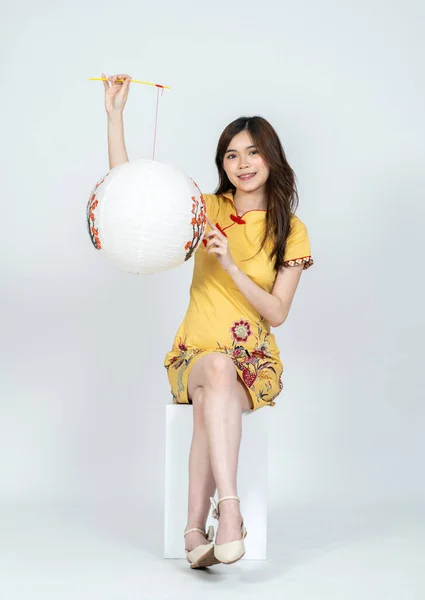 A young beautiful asian woman smiling with simple chinese yellow dress holding a white lantern, with isolated white background