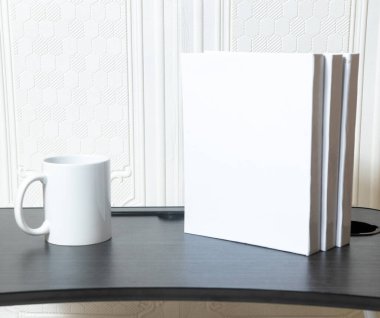 A couple of standing white colored hardcover books on the top of a black table and some decorations arranged around it, hardcover mockup template image