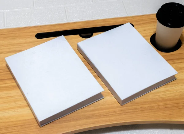 A couple of the white colored hardcover books laying out on the top of a table with wooden texture and some decorations arranged around it