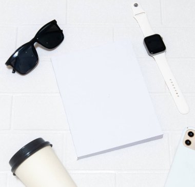 A white colored cover book laying out on the top of a white colored brick mat with a glasses and blank smartwatch, hardcover mockup template image