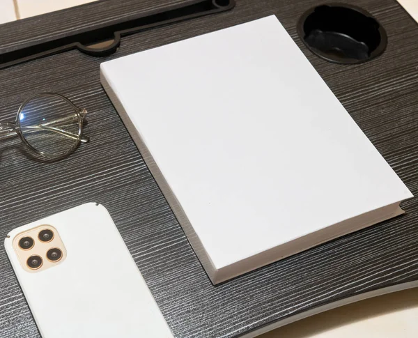 A white blank hardcover book laying on the top of a black table with a phone near it, hardcover mockup template image