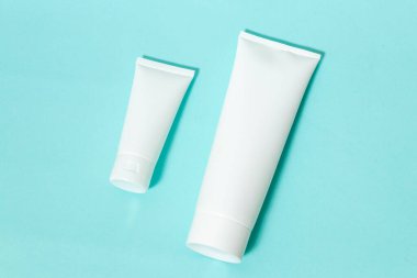 Two white colored cream bottle laying out next to each other on the top of a blue paper, bottle mockup template image