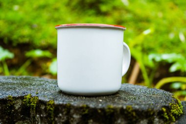 An enamel mug standing on the top of a cement floor with out of focus scenic background, enamel mug mockup image