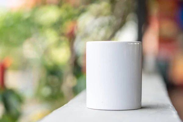 A blank white tea mug standing on the top of a fence with the blurred out colorful background, coffee mug mockup image