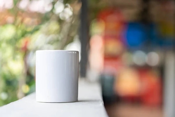A blank white tea mug standing on the top of a fence with the blurred out colorful background, coffee mug mockup image