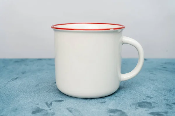 A white blank enamel mug standing out on top of a blue cloth minimalist concept, enamel mug mockup image