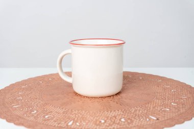 A white blank enamel mug on the top of a rounded mat decorated with the white background, enamel mug mockup image