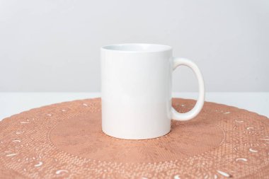A white blank coffee mug on the top of a rounded mat decorated with the white background, coffee mug mockup image