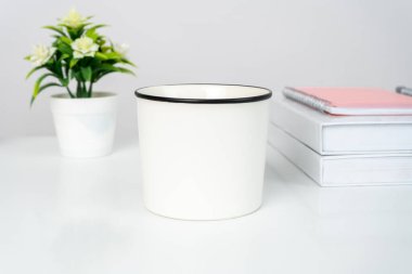 A white blank coffee mug on the top of a white table decorated with minimalistic style, enamel mug mockup image