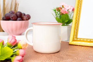 A white blank enamel mug on the top of a rounded mat decorated with simple stuff around it, enamel mug mockup image