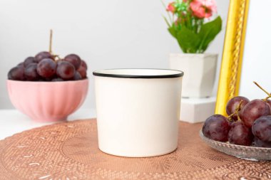 A white blank enamel mug on the top of a rounded mat decorated with simple stuff around it, enamel mug mockup image