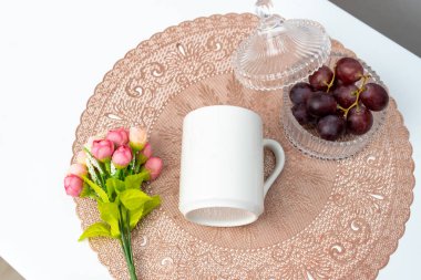 A white blank coffee mug on the top of a rounded mat decorated with simple stuff around it, coffee mug mockup image