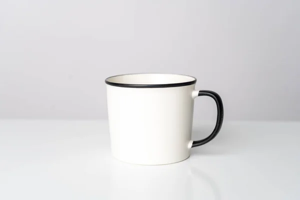A white blank enamel mug on the top of a white table with a white background, enamel mug mockup image