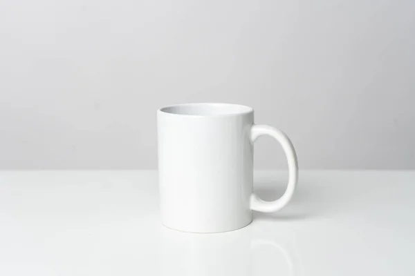 A white blank coffee mug on the top of a white table with a white background, coffee mug mockup image