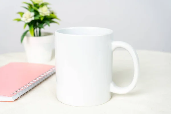 A white blank coffee mug on the top of a white table decorated with minimalistic looks, coffee mug mockup image