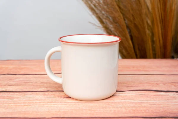 A white blank enamel mug on the top of a wooden texture mat with minimalistic looks, enamel mug mockup image