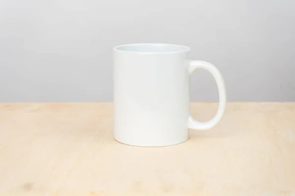 A white blank coffee mug on the top of a plywood with a clean white background behind it, coffee mug mockup image