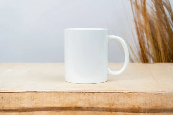 A white blank coffee mug on the top of a plywood with some simple rustic flower at the background, coffee mug mockup image