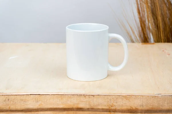 A white blank coffee mug on the top of a plywood with some simple rustic flower at the background, coffee mug mockup image