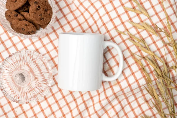 A white blank coffee mug on the top of a hand cloth decorated with simple stuff around it, coffee mug mockup image