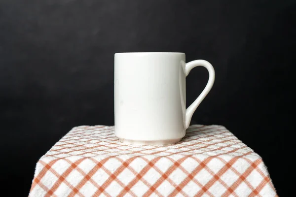A white blank coffee mug on the top of a hand cloth isolated with black color as the background, coffee mug mockup image