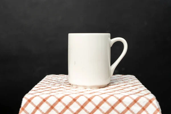 A white blank coffee mug on the top of a hand cloth isolated with black color as the background, coffee mug mockup image