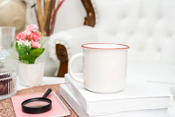 A white blank enamel mug standing out on a white book with some decorations placed around it, enamel mug mockup image