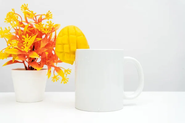 A white blank coffee mug with a piece of small mango decorated to the edge of the mug, minimalist fresh concept, coffee mug mockup image