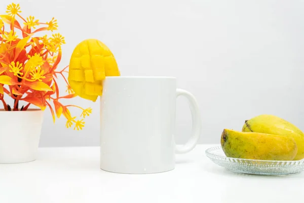 A white blank coffee mug with a piece of small mango decorated to the edge of the mug, minimalist fresh concept, coffee mug mockup image