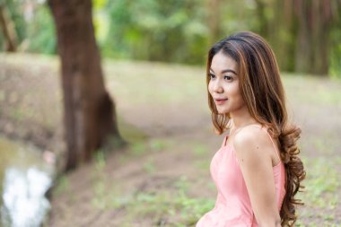 Young woman in pink dress, bokeh park background perfect for relaxation, with negative space for copy