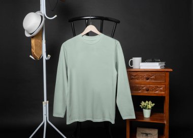 A blank dusty blue shirt hanged on to a chair with minimalist decorations, on a black background, shirt mockup image