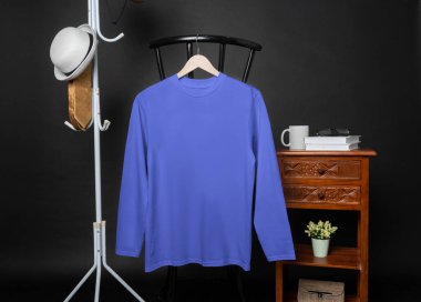 A blank blue shirt hanged on to a chair with minimalist decorations, on a black background, shirt mockup image