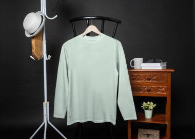 A blank mint shirt hanged on to a chair with minimalist decorations, on a black background, shirt mockup image