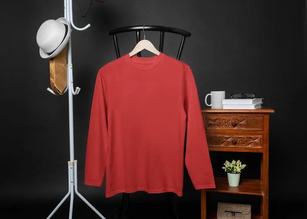 A blank red shirt hanged on to a chair with minimalist decorations, on a black background, shirt mockup image