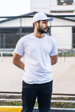 Bu resim modern erkekliğin özünü yakalar, sakallı bir adam beyaz bir gömlek ve şapka, beyaz boş bir şapka ve gömlek modeli bir resimle güvenle poz verir.