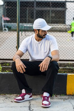 Beyaz gömlekli adam şık bir şekilde oturuyor. Tenis kortunun arka planında, beyaz şapkası ve tişört modeli imajı var.