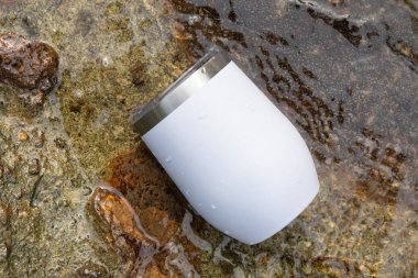 Bir görüntü, sakinliğin ve gevşemenin özünü yakındaki bir nehrin nazik akışına düşünceli bir şekilde yerleştirilmiş beyaz bir şarap kadehiyle yakalar.