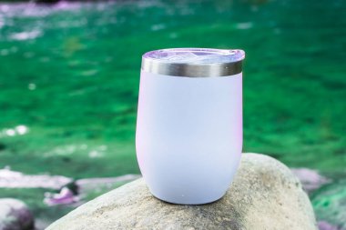 Huzur ve sükunetin özünü kusursuz bir şekilde yansıtan, dingin bir nehrin kenarında beyaz bir şarap bardağı.