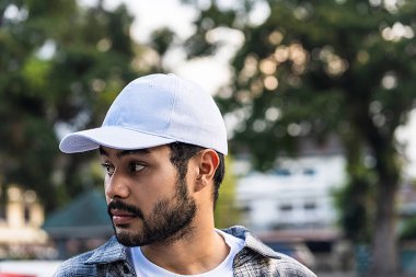 Bu çarpıcı görüntü, temiz ve taze beyaz bir şapka giyen sakallı bir adamın özgüvenli ve güçlü bir duruş sergilediğini gösteriyor.