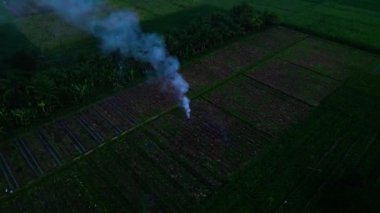 Dairesel hareketlerle çekilen bir hava görüntüsü, siyah bir ortamda yanan pirinç kabuklarından çıkan dumanı gösteriyor.