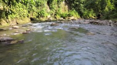 Su dalgalanmalarını ve çakıl taşlarını gösteren akan suyun alçak irtifa görüntüsü.