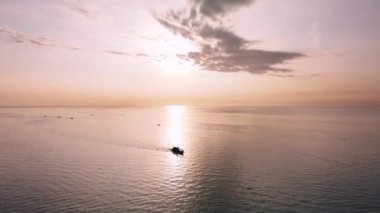 Okyanusta bir teknenin siluetini takip eden ve arka planda güneş doğarken bir dron tarafından çekilen hava görüntüleri.