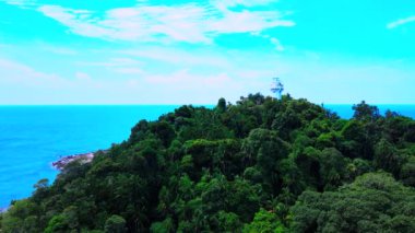 Bir deniz fenerinin uç kısmının görüntüsü yoğun yeşil ormandan daha uzundur. İnsansız hava aracı ile çekilmiştir.