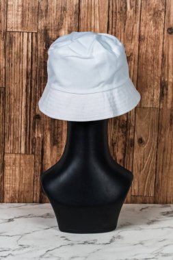 Büyüleyici bir maket görüntüsü, minimalist bir düzende bir moda oyuncağı tarafından zarif bir şekilde takılmış boş bir kova şapka sergiliyor.