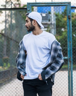 Büyüleyici bir tasvirde, kendine güveni ve tarzı olan, beyaz, boş bir şapka ve gömlek giyen, minimalist bir düzende genç bir adam var.