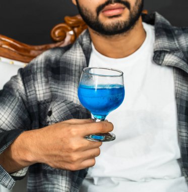 Biraz karizmayla, bir maket görüntüsü sunar. Şarap içen genç bir adam.