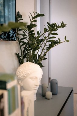 Beyaz göğüslü bir kadın bir bitkinin yanındaki masada oturuyor..