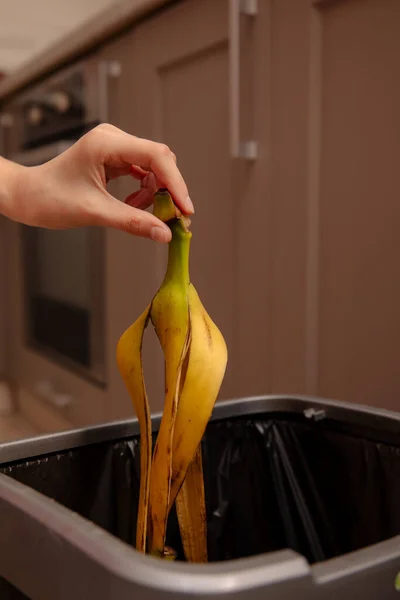 Woman putting banana peel in a trash bin. Kitchen and home