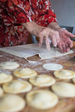 Unrecognizable aged woman cutting puff pastry with a glass to prepare dumplings. Spain